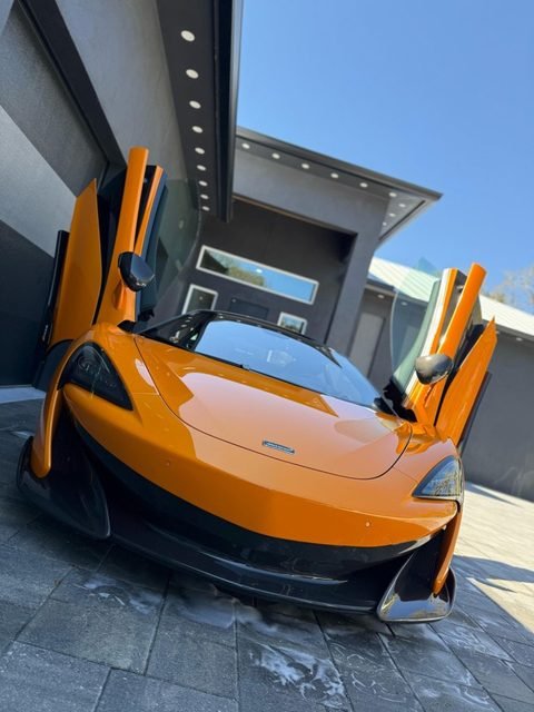 Mobile car detailing service performed on an orange sports car in a driveway